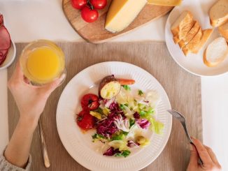 A top-view of a delicious breakfast setting featuring a salad, bread, cheese, tomatoes, and orange juice.