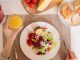 A top-view of a delicious breakfast setting featuring a salad, bread, cheese, tomatoes, and orange juice.